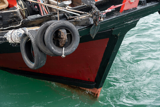 Close-up of the red and black wooden prow of a classic Chinese sampan boat equipped with rubber tire bumpers and an anchor resting in green water.