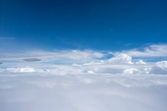Expansive horizontal landscape of an airplane wing slicing through open airspace above a continuous blanket of fluffy white clouds.