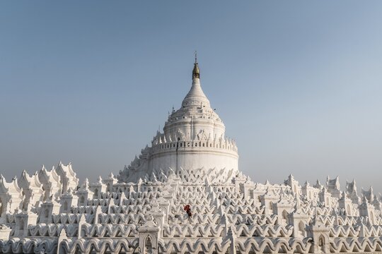 Buddhist monk stands with red umbrella in front of Hsinbyume Pagoda, Mingun, Myanmar