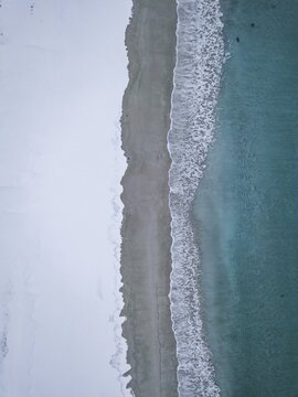 Haukland beach from above, turquoise sea water borders on snow surface, drone shot, Lofoten, Norway