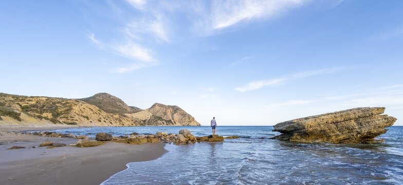 Young man standing on a rock, sandy beach with rocky cliffs, Paralia Paradisos, Kos, Dodecanese, Greece