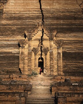 Buddhist monk stands with red umbrella in the entrance of Mingun Pagoda, Mingun, Myanmar