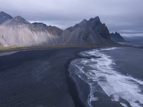 Aerial view, black lava edge with sea surf with mountain Vestrahorn, Cape Stokksnes, bay Hornvik, southeast Iceland, Iceland