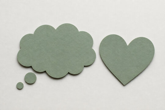 Two flat, sage green shapes, a thought bubble and a heart, are displayed against a plain light background.