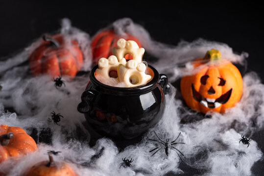 Spooky Halloween cauldron filled with ghost shaped cookies surrounded by pumpkins and spiderwebs
