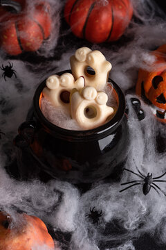 Spooky Halloween Candy Treats in Black Cauldron Surrounded by Cobwebs and Pumpkins for Festive Celebration