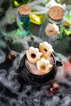 Spooky Halloween cauldron filled with ghost shaped candy and surrounded by potion bottles and cobwebs