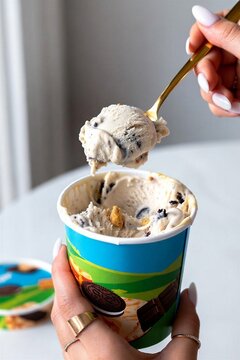 Woman holding ice cream scoop with cookie dough flavor in container  