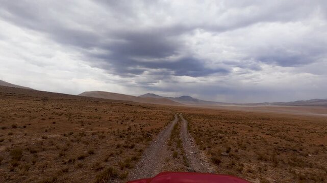 View while driving down a dirt road in the wide open desert in Utah as wind blows dust in the distance.