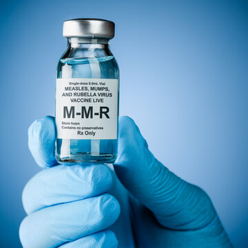 Nurses hand in blue medical gloves holding a vaccine bottle with MMR text. Health care concept of prevention or treatment of measles, mumps, and rubella viruses.