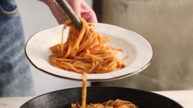 Fresh spaghetti bolognese lifted from a frying pan and placed onto a clean elegant plate held in the air, capturing the final serving process before an Italian meal is ready for the table