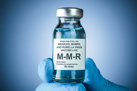 Nurses hand in blue medical gloves holding a vaccine bottle with MMR text. Health care concept of prevention or treatment of measles, mumps, and rubella viruses.