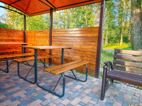 Covered park gazebo with wooden tables, benches and decorative railings, situated on a tiled area.