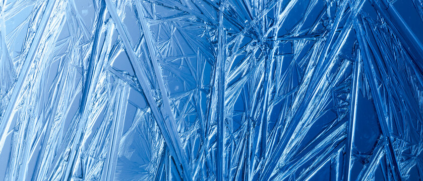 Ice frozen in intricate patterns of delicate crystals with brilliant contrasts of deep blues. Real unique patterned crystal formations. Sparkling window frost or icy cold winter frosting background.
