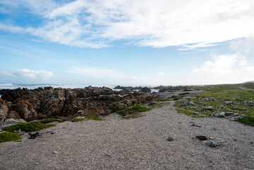 Obraz premium Gravel trail extends along the rugged rocky shoreline under a cloudy sky at Cape Agulhas in the Western Cape region of South Africa.