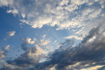 Fototapeta premium Dreamy clouds dance across a vibrant sky at sunset, casting golden rays as day transforms into night with hues of blue and orange mingling in the horizon