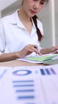 Asian businesswoman calculating financial data and analyzing reports in office.