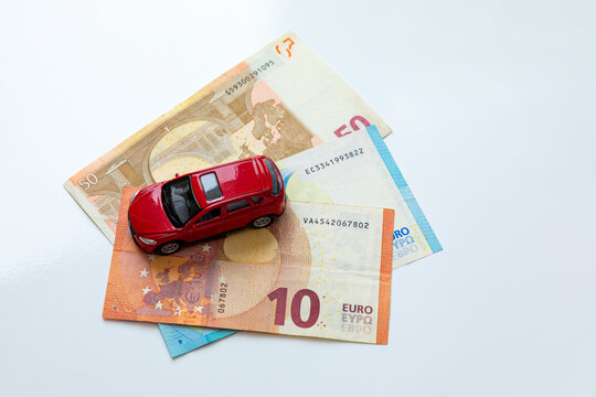 Red toy car placed on top of Euro banknotes, including 10, 20, and 50 Euro denominations, arranged on a white background. Car insurance, purchase and loan concept. copy space