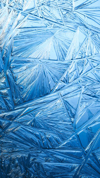 Ice frozen in intricate patterns of delicate crystals with brilliant contrasts of deep blues. Real unique patterned crystal formations. Sparkling window frost or icy cold winter frosting background.