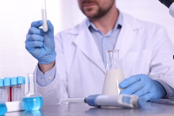 Fototapeta premium Quality control. Scientist in gloves examining milk at table in laboratory, closeup
