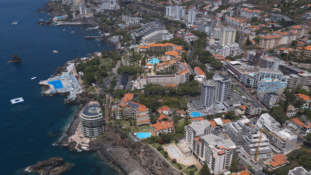 Funchal, Portugal - 15 August 2026: Aerial view of the coastal city of Funchal in Madeira, featuring hotels, swimming pools, rocky cliffs, and the Atlantic Ocean.