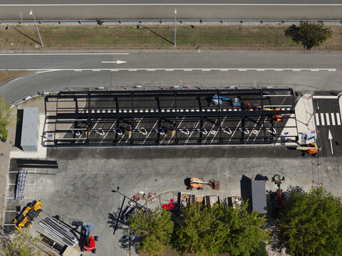 Portugal - 14 August 2026: Aerial view of an electric vehicle charging station under construction, featuring a metal frame structure, marked parking bays, and construction equipment.