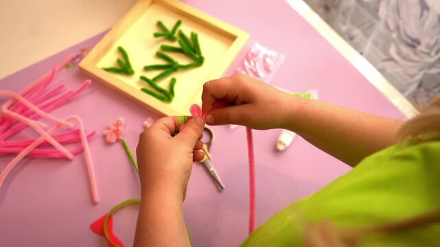 Close-up POV of small children hands folding soft pipe cleaner wires into a flower shape for a mother day handmade gift decoration under social educational program guidelines