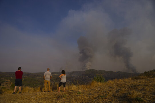 Torre de Moncorvo, Portugal - 20 August 2026: View of three people standing on a hill observing a wildfire with large smoke plumes rising over the landscape.