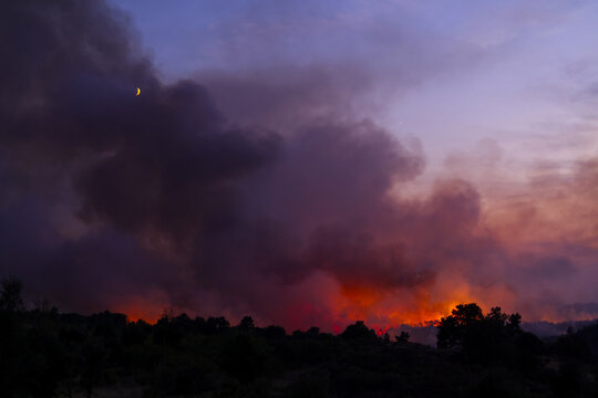 Torre de Moncorvo, Portugal - 20 August 2026: View of a wildfire burning at night with thick smoke and glowing orange flames under a crescent moon.