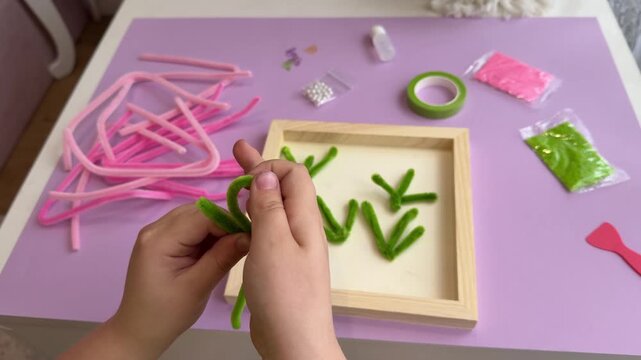 POV look of a toddler twisting pink and green chenille stems into an artistic shape for sensory integration therapy or preschool art class presentation backdrop