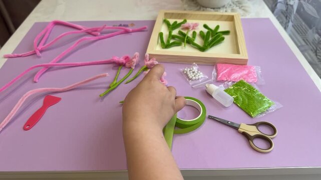 Top view of small child hands carefully adjusting soft pipe cleaner petals inside a wooden frame template for an interactive kindergarten arts and crafts learning course
