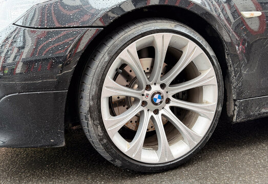 Close-up of original silver multi-spoke BMW Style 166 alloy wheel rim on a black 5 Series E60 sedan car. Premium German automobile parts with high-performance brake rotor and a dirty tire after rain. 