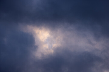 Obraz premium Heavy dark storm clouds frame a bright opening of sunlight, creating a dramatic, atmospheric sky with rich navy blue and golden highlights—ideal background for powerful nature design concepts.