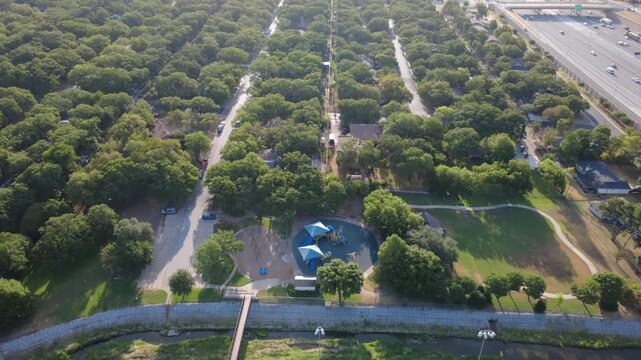 Canopied playground structures provide shaded family gathering spots near Little Bear Creek. Stone drainage channels, footbridges, asphalt lots support neighborhood leisure, Hurst, Texas