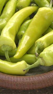 Close-up of Hungarian Hot Wax peppers on a handmade dish. Fresh, whole light-yellow chili pile on a brown plate. Table spin, vertical video.