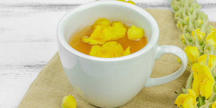 Cup of herbal tea with mullein flowers and leaves on neutral wooden background. Natural light