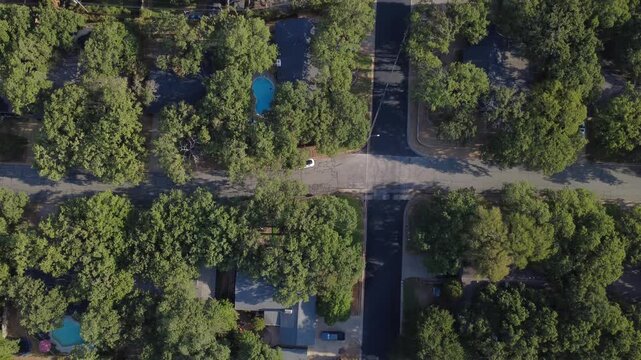 Fresh asphalt roadway junctions intersect shaded residential corridors near Little Bear Creek. Parked vehicles, secluded swimming pools, heavy live oak branches show local character, Hurst, Texas
