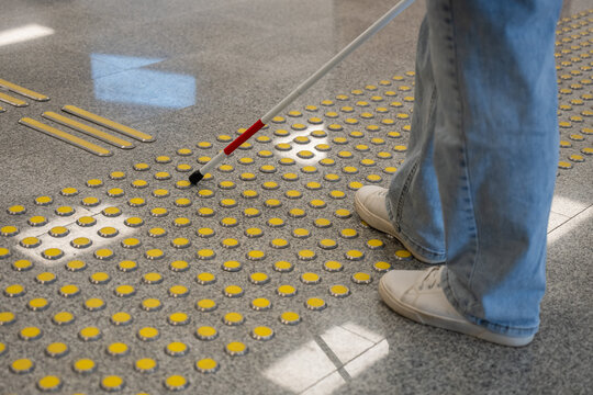 A blind woman walks on tactile paving. Close-up of her feet and a walking stick.