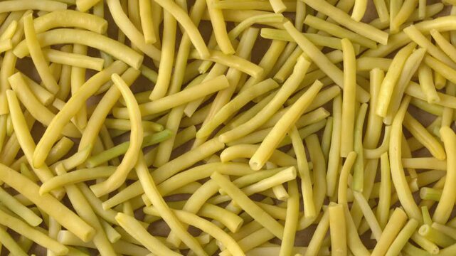 Top view of cut yellow wax beans, full-frame background texture. Fresh organic Golden Teepee beans chopped for pickling, slowly rotating with backlit natural window light.
