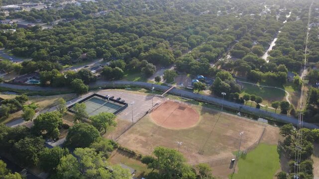 Spacious baseball diamonds welcome local community sports leagues beside Little Bear Creek. Outdoor courts, open lawns, perimeter tree canopies display active recreation grounds, Hurst, Texas
