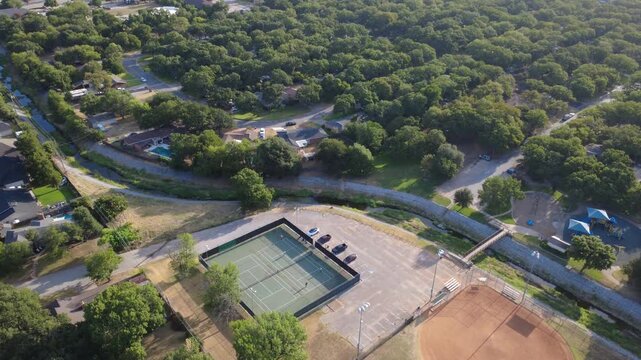 Regulation tennis courts occupy public recreation acreage alongside Little Bear Creek waterway. Marked parking stalls, pedestrian bridges, shaded banks supply neighborhood recreation, Texas