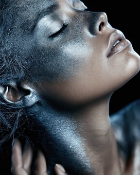 Woman with metallic silver face and body paint in dramatic studio portrait against a black background.