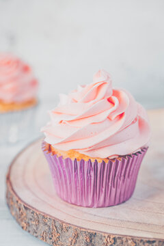 Close-up of a cupcake  on a wooden chopping board with pink buttercream icing