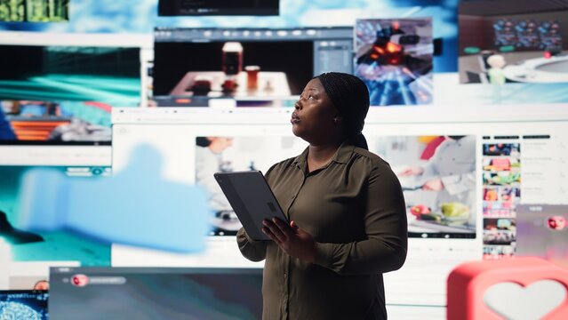 Woman uses a tablet to receive personalized video recommendations delivered instantly; African American user enjoys social media content with unlimited streaming opportunities on the device.