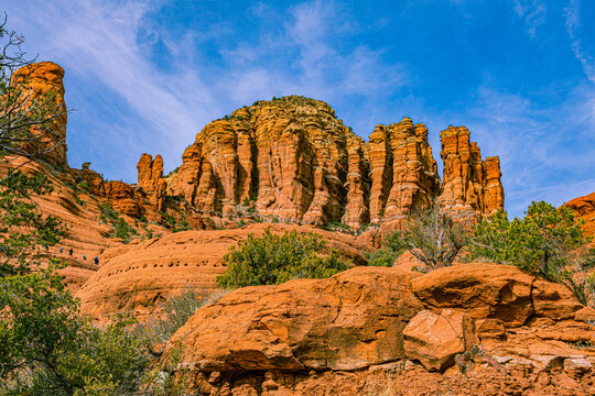 Hikers ascending the scenic red sandstone rock spires and towers under a clear blue sky along Cathedral Rock Trail in Sedona, Arizona.