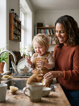 Mother and toddler wash dishes together in kitchen