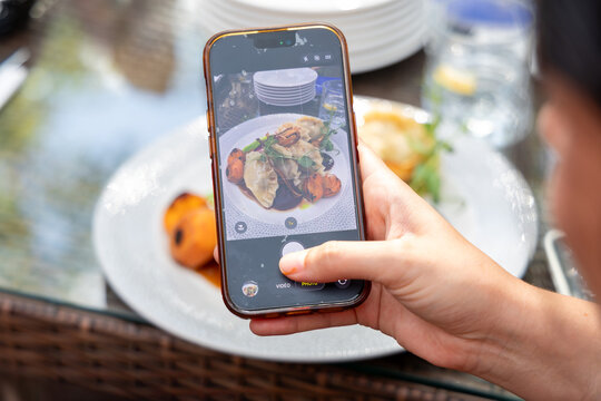 Woman taking photo of restaurant food with smartphone camera for social media sharing close up holding mobile phone taking picture of dinner dish.