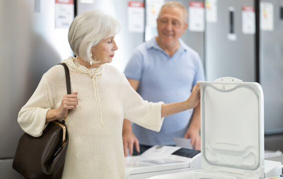 Selective elderly couple choosing top-loading washing machine at household appliances store with large assortment