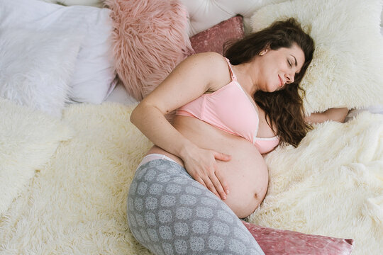 Pregnant woman sleeping peacefully on bed with plush pillows, touching big belly, cozy rest and maternity comfort at home.