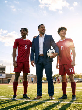 Vertical portrait of a manager in a suit holding a soccer ball with two players in red uniforms. Proud coach standing with athletes on a football field. Sports teamwork and leadership concept